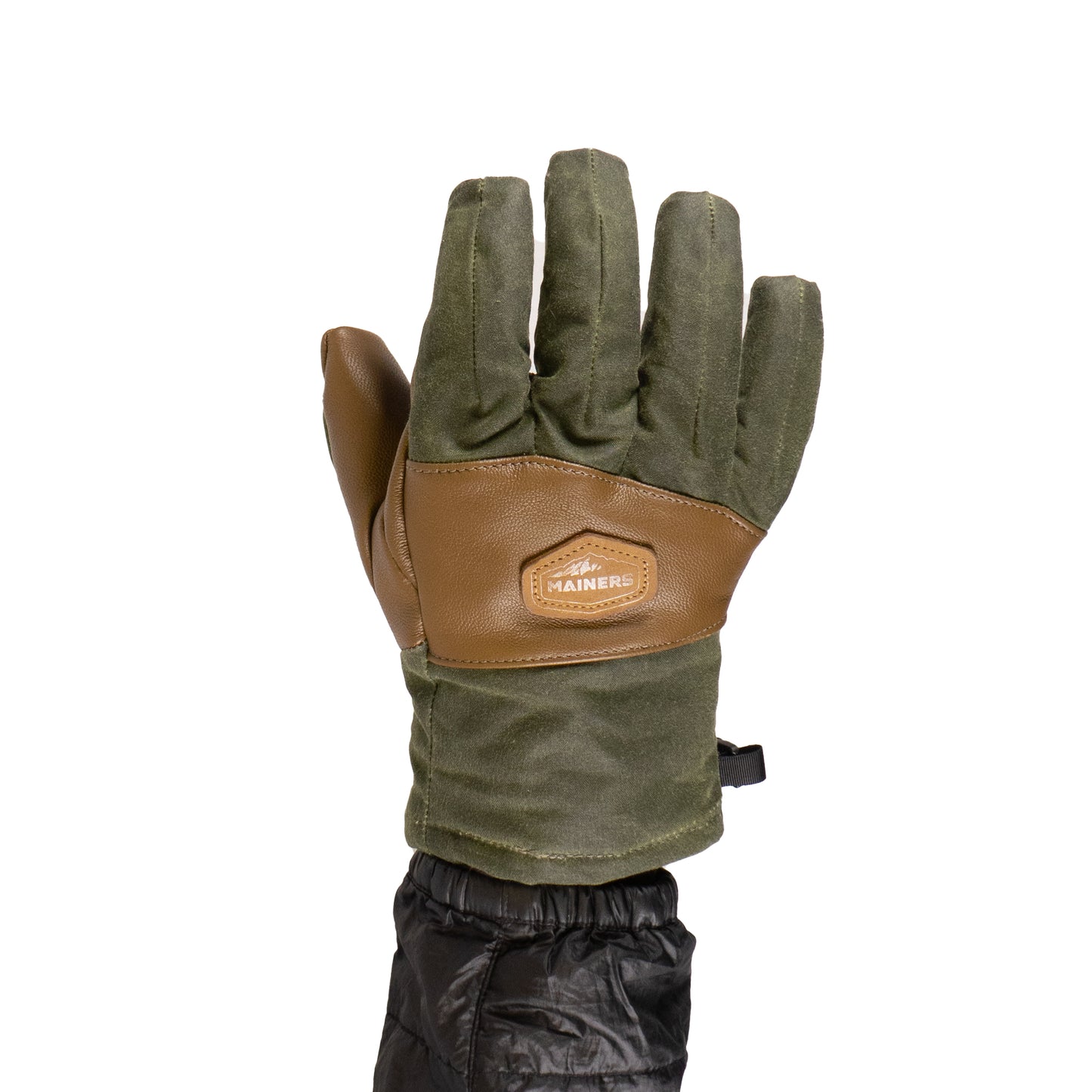 A person in a black jacket wears Mainers' MT Battie Glove in green and brown, featuring a logo patch on the back and a durable leather palm for enhanced grip.