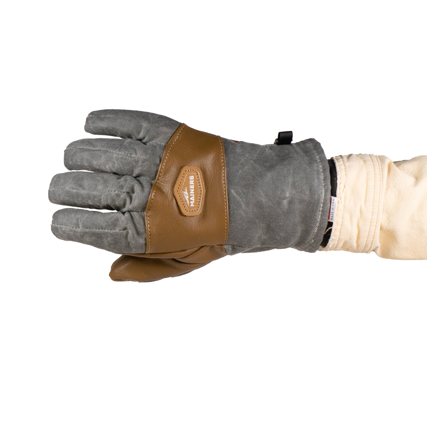 An outstretched hand flaunts the versatile Ragged MT Glove by Mainers, designed with grey fabric and brown leather, set against a white background—ideal for winter adventures.