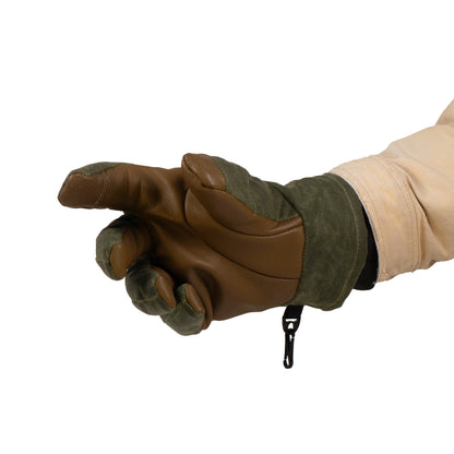 A hand in a Mainers Ragged MT Glove, crafted from rugged waxed canvas and leather in brown and green, makes an extended pointing gesture against a plain background.